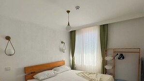 Une chambre à coucher avec un lit en bois, une table de chevet, une lampe suspendue, une fenêtre avec des rideaux et une armoire en bois.