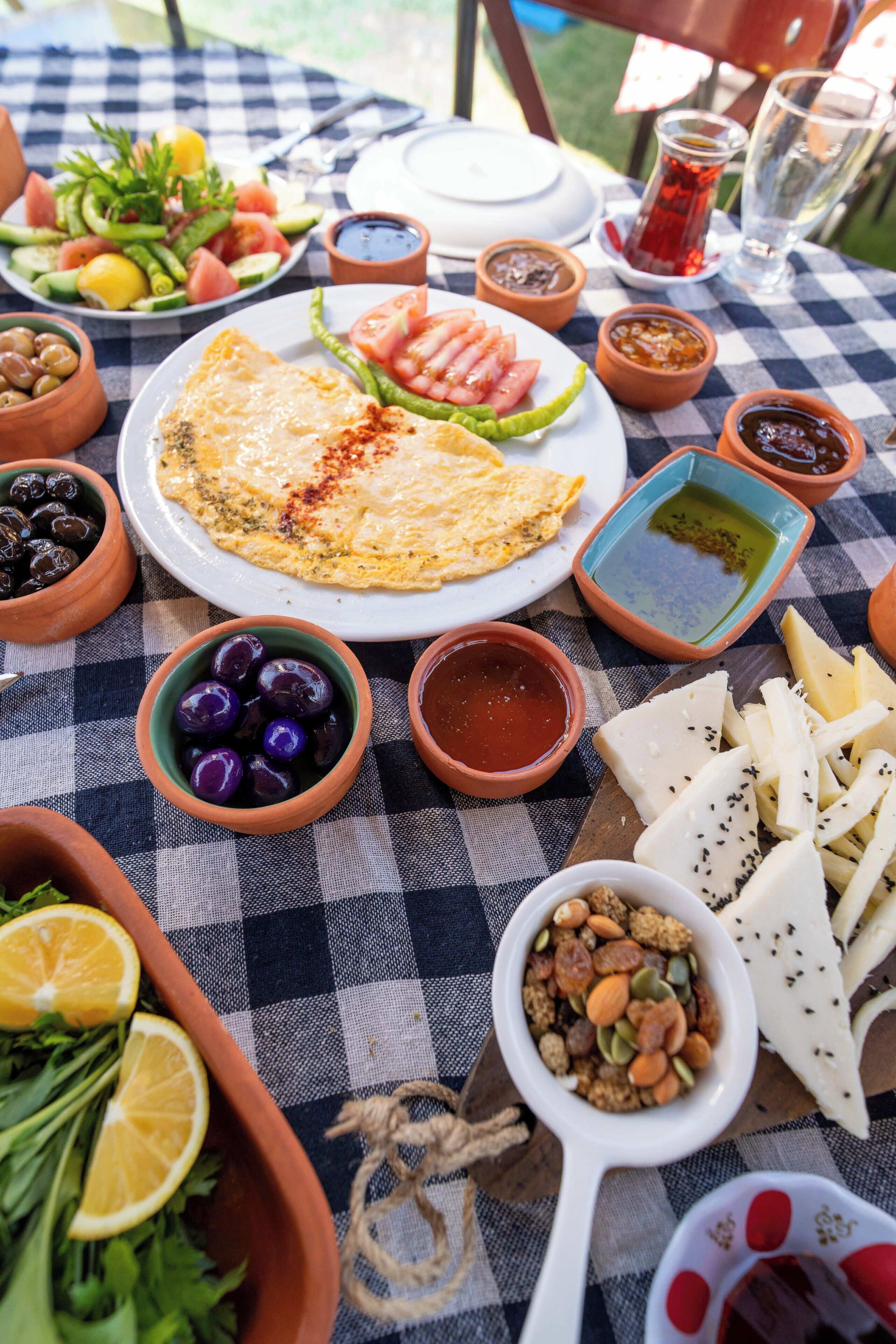 A table set with various dishes including a salad, cheese, olives, and a plate of sliced tomatoes and green peppers.