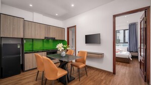 Une cuisine moderne avec un coin repas, un téléviseur à écran plat et une chambre à coucher visible à travers une porte ouverte.