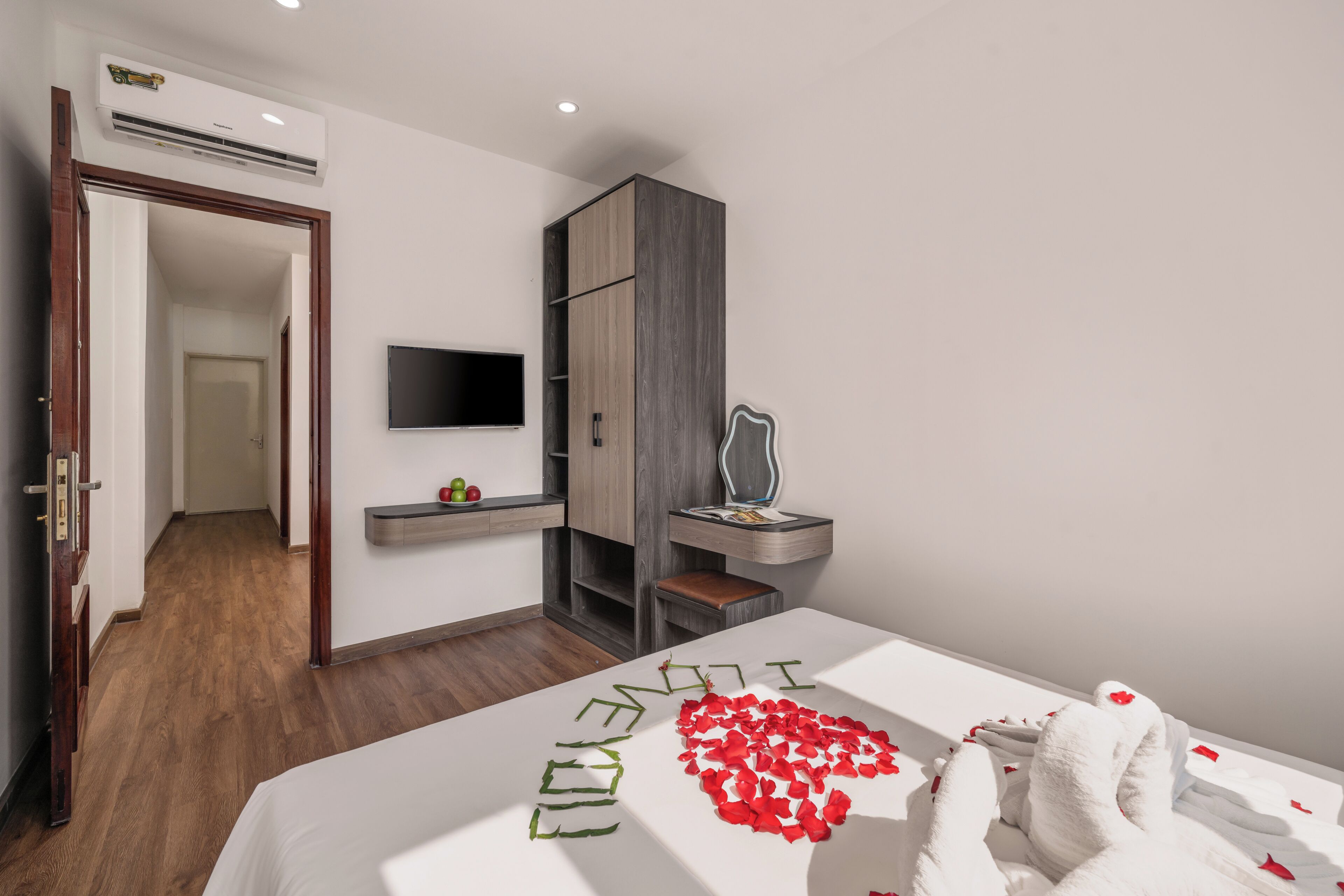 A modern hotel room with a bed, a TV, a wardrobe, and a desk with a chair.
