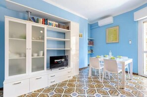 Ein Zimmer mit einem weißen Schrank mit Glastüren, einem Flachbildfernseher, einem Esstisch mit Stühlen und einem gemusterten Boden.