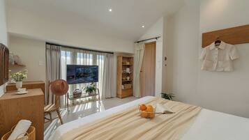 Quarto de hotel moderno com uma cama grande, televisão, secretária e guarda-roupa.
