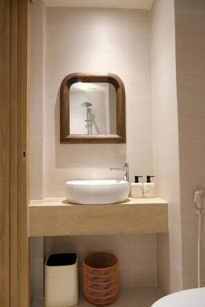 Un baño con un lavabo blanco, un espejo con marco de madera y una cesta de mimbre.