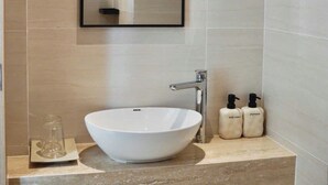 Un baño con un lavamanos blanco tipo recipiente, un espejo y dos botellas de champú y gel de baño.