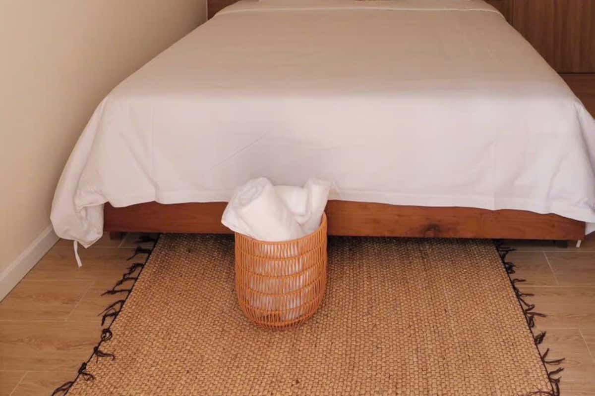 A single bed with a wooden headboard, a woven basket at the foot of the bed, and a door to the right.