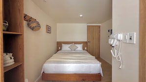 Un dormitorio con estructura de cama de madera, ropa de cama blanca, un secador de pelo montado en la pared y un estante con toallas dobladas.