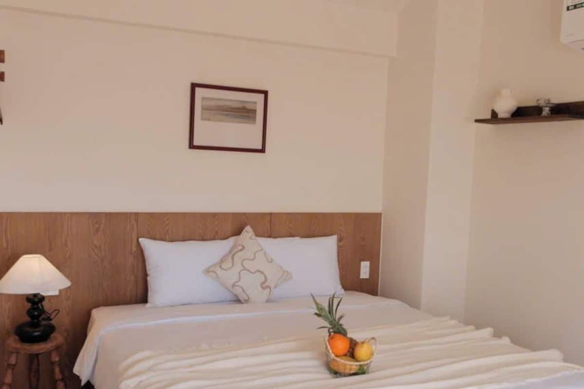 A neatly made bed with a white bedspread, a small bedside table with a lamp, and a fruit basket on the bed.