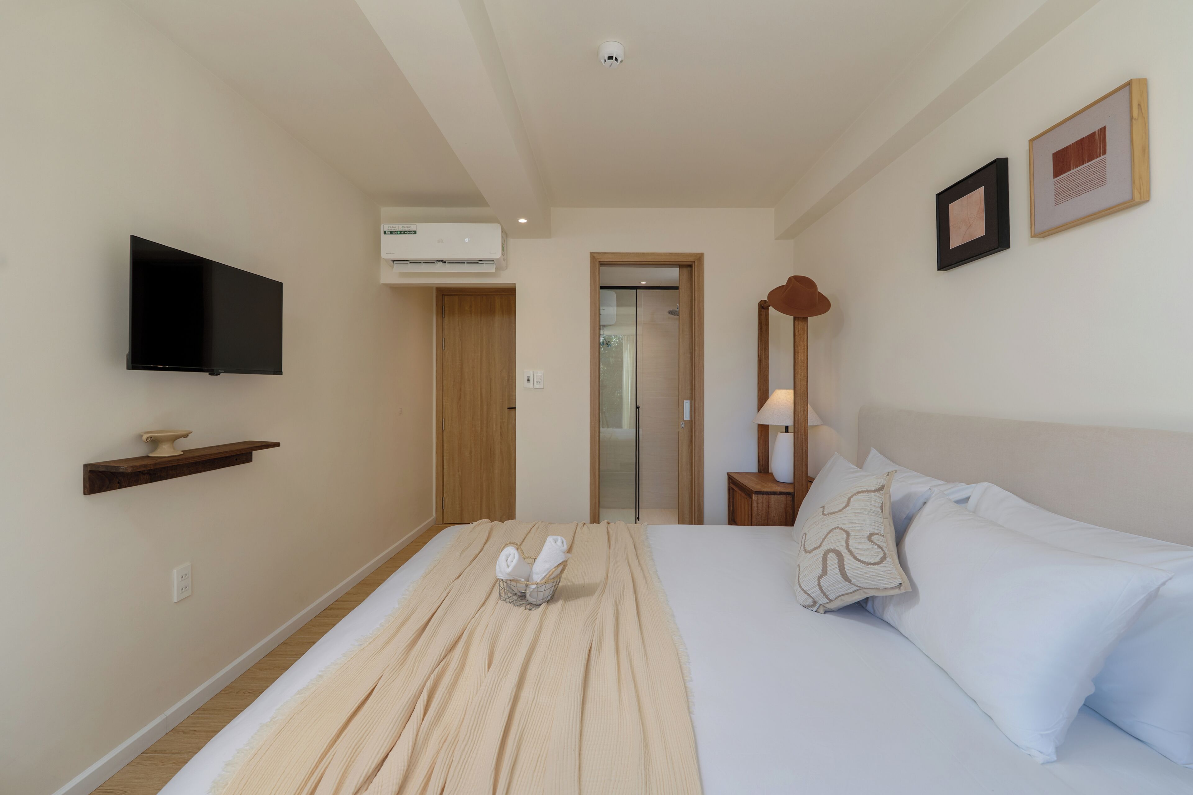 Een hotelkamer met een bed, een aan de muur bevestigde televisie, een houten plank en een deur naar een andere kamer.