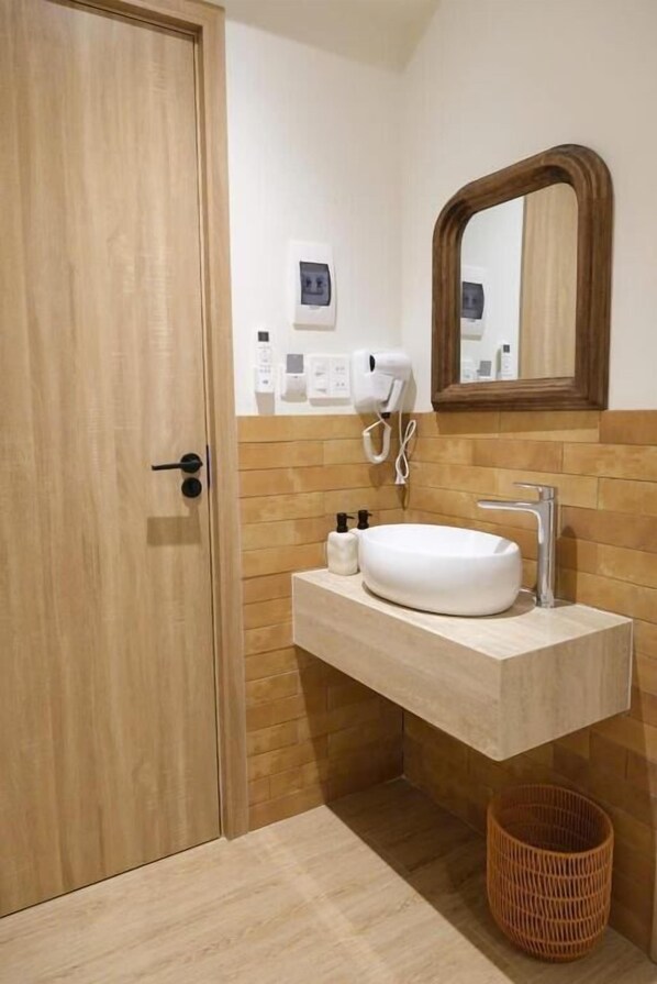 Un baño con puerta de madera, un lavabo blanco, un espejo y un secador de pelo montado en la pared.