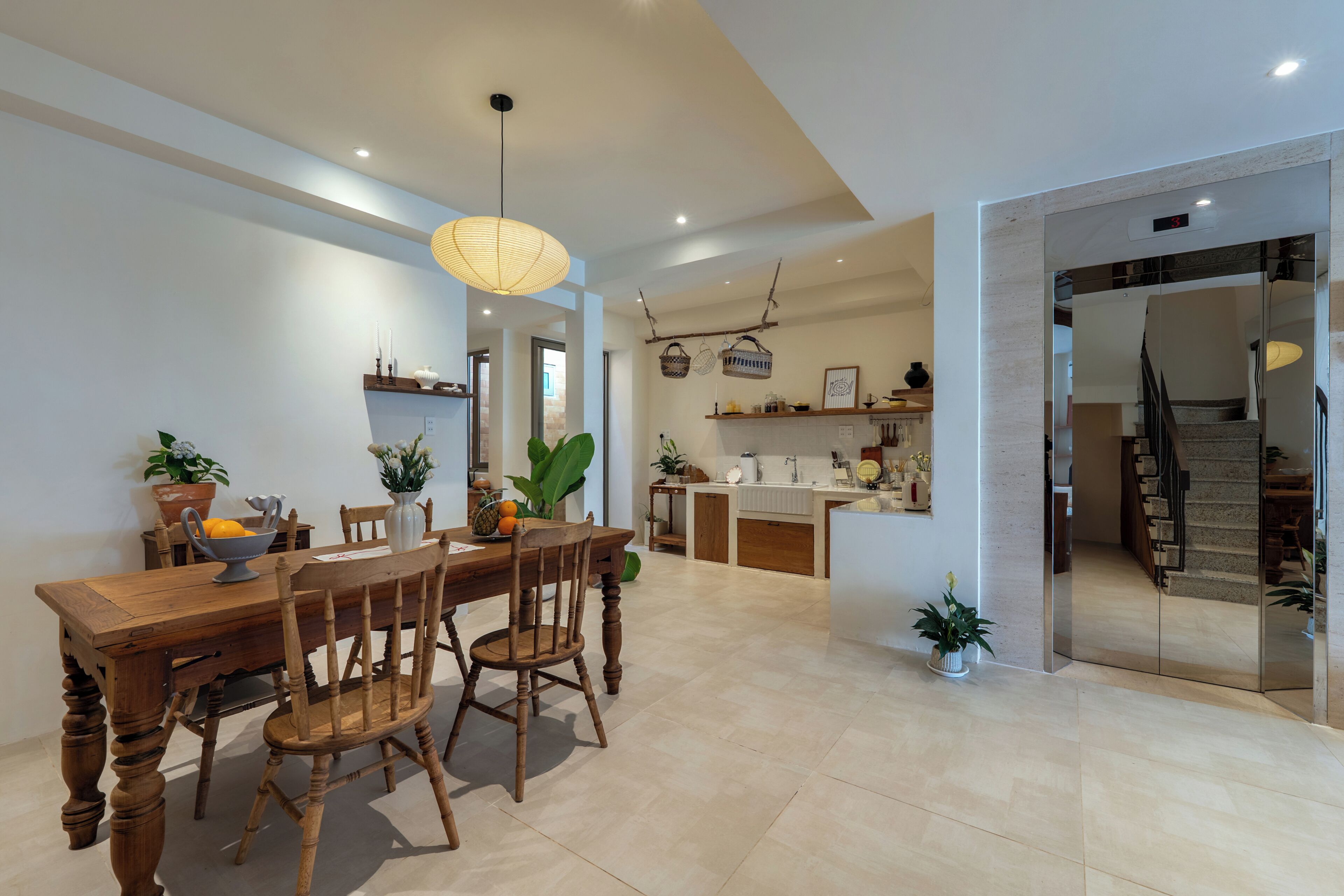 A spacious dining area with a wooden table and chairs, a hanging light fixture, and a view into the kitchen area.