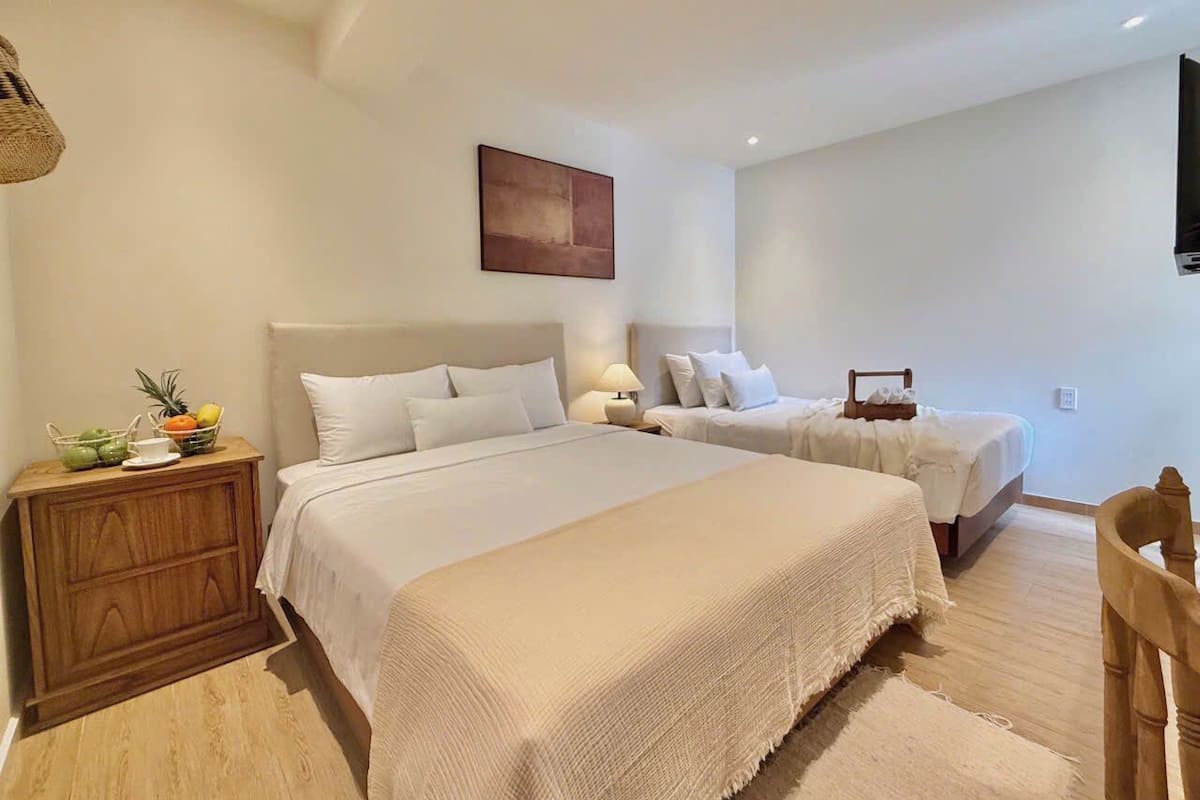 A bedroom with a large bed, a smaller bed, a wooden nightstand, a lamp, and a fruit basket.