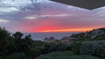 Un paysage côtier avec un coucher de soleil, un terrain rocheux et une végétation luxuriante.