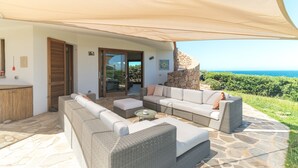 Un espacio al aire libre con mobiliario de mimbre, suelo de piedra y vista al mar.