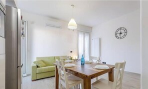 Un comedor con mesa de madera, sillas, sofá verde y un reloj en la pared.