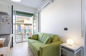 En moderne stue med en grøn sofa, et lille bord med en lampe, og en skydedør, der fører ud til en altan.