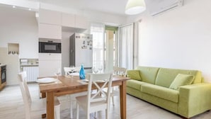 Une cuisine moderne avec des meubles blancs, une table à manger en bois et un canapé vert.