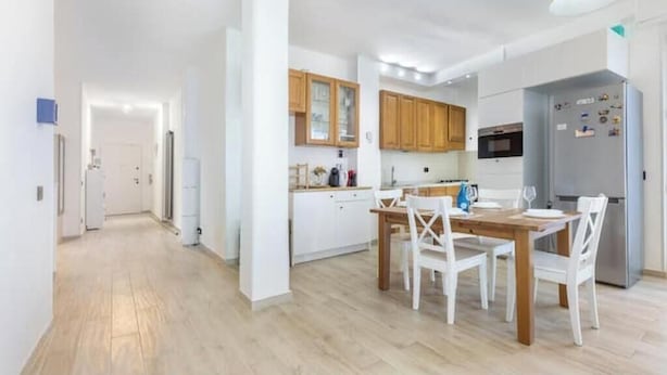 Une cuisine moderne avec des meubles blancs, une table à manger avec des chaises et un réfrigérateur.
