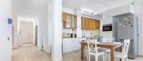 A modern kitchen with white cabinets, a dining table with chairs, and a refrigerator.