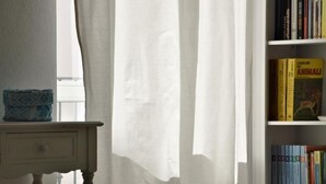 A room with a bookshelf, a small table, and a window with sheer curtains. - Palau Noal (Alghero)