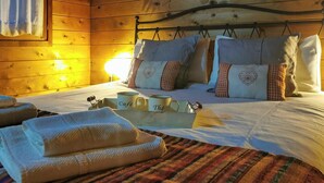 Una habitación acogedora con una cama, almohadas, una mesita de noche con tazas y un ventanal con cortinas.