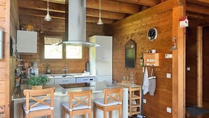 Cocina de cabaña de madera con una isla central, sillas de madera, un fregadero, armarios y un reloj en la pared.