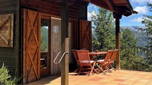 Una cabaña rústica con un porche cubierto, muebles de madera y cimientos de piedra.