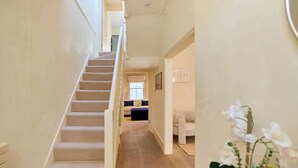 Una escalera conduce a una habitación con una cama, un ventanal y una planta.