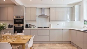 Una cocina moderna con electrodomésticos integrados, una zona de comedor con una mesa dispuesta para cuatro personas, y un amplio ventanal que proporciona luz natural.