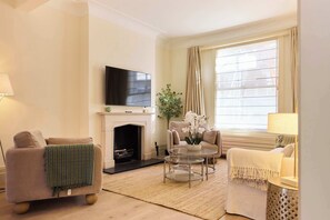 A living room with a fireplace, sofa, armchair, and a television. - The Arch & Lightwell - Chelsea (London)