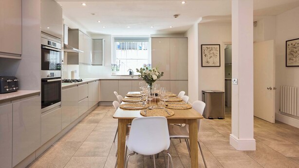 Una cocina moderna con electrodomésticos integrados, una mesa de comedor preparada para seis personas y vistas del área de estar contigua.