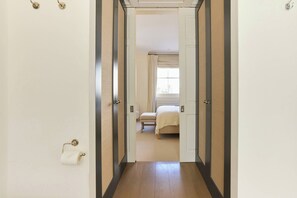 A hallway leading to a bedroom with a bed, a window with curtains, and a toilet paper holder. - The Arch & Lightwell - Chelsea (London)