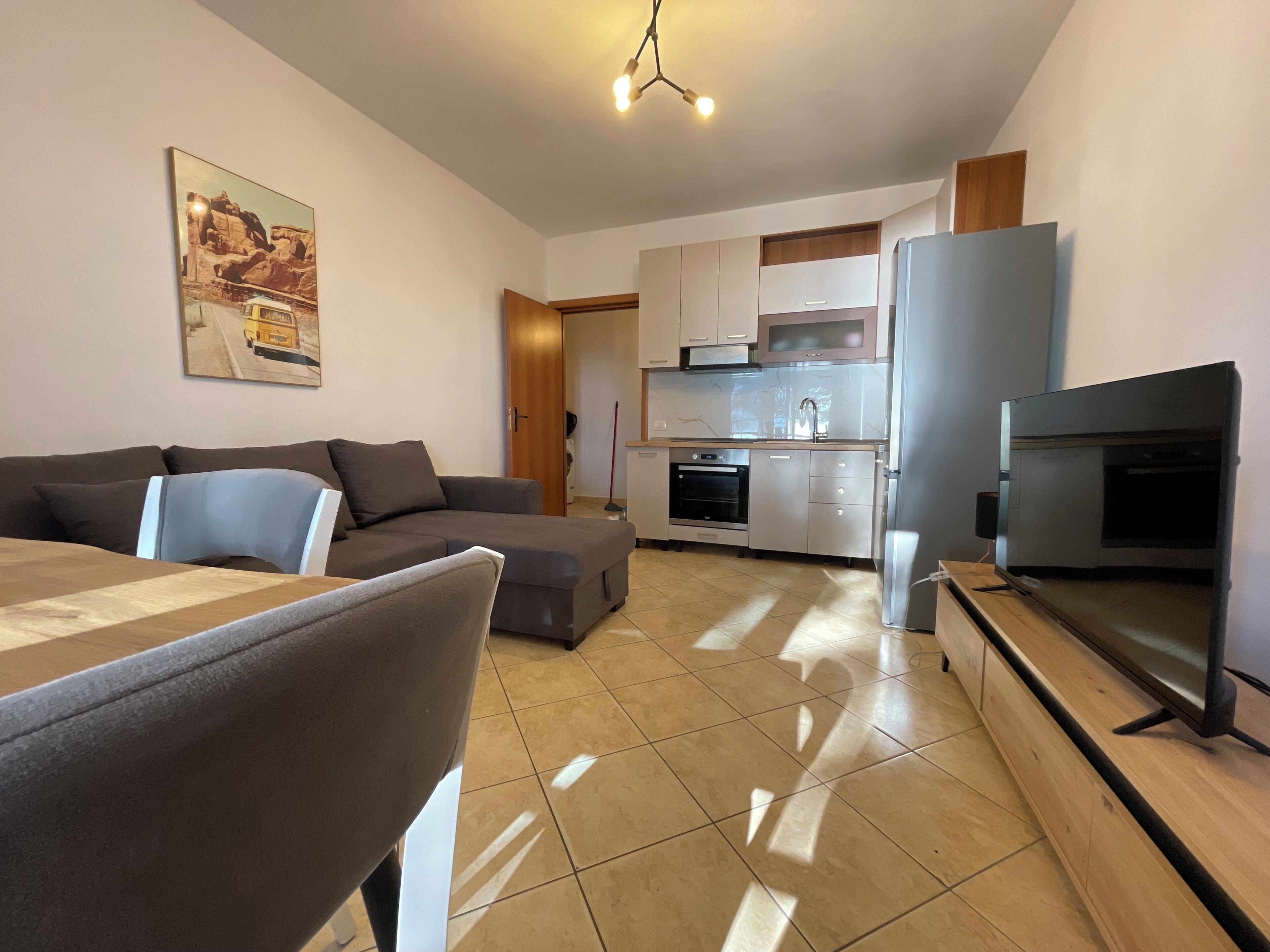 A modern living room with a sofa, a dining table, and a kitchen area with a refrigerator, oven, and microwave.