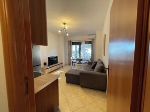 Ein modernes Wohnzimmer mit Fernseher, Sofa, Essbereich und großen Fenstern.