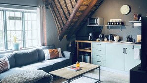 Een gezellige woonkamer met een bank, salontafel en een keukenhoek met een magnetron en kasten.