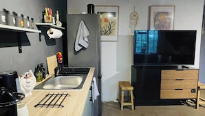 Een moderne keuken met een ingebouwde kookplaat, spoelbak en een houten aanrecht. Er staat een klein krukje, een televisie en een plank met keukenspullen.