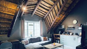 Een knus loft-achtig woongedeelte met een schuine plafond, een bank, een salontafel, een kitchenette en een eethoek.