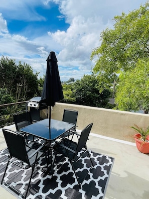 Un patio al aire libre con mesa y sillas, una parrilla y una planta en maceta.