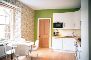 Een keuken met witte kasten, een magnetron en een houten deur.