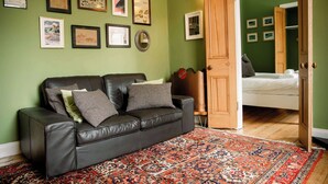 A room with a black leather sofa, a patterned rug, and a door leading to a bedroom with a bed. - 1BR unit near Greyfriars Church with garden views (Edinburgh)