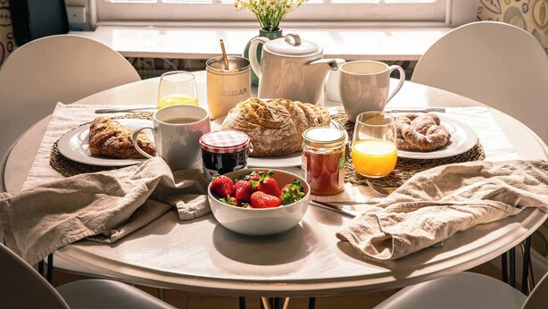 A breakfast table with pastries, a bowl of strawberries, a pitcher, a mug, and a glass of orange juice. - 1BR unit near Greyfriars Church with garden views (Edinburgh)