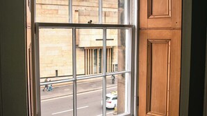A window with a view of a street and a building, a radiator below, and wooden paneling on the wall. - 1BR unit near Greyfriars Church with garden views (Edinburgh)