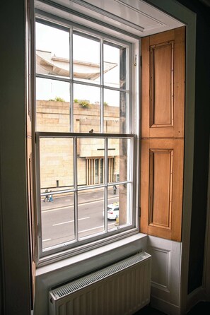 A window with a view of a street and a building, a radiator below, and wooden paneling on the wall. - 1BR unit near Greyfriars Church with garden views (Edinburgh)