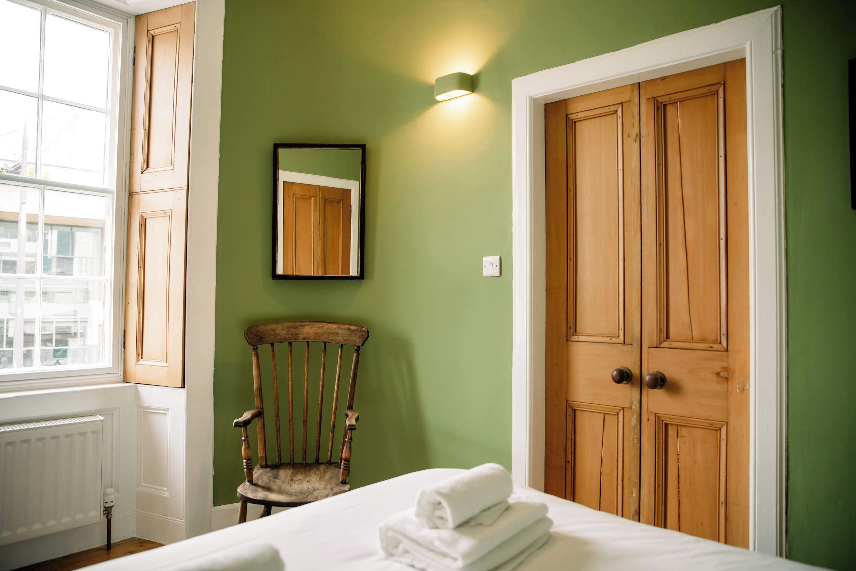 A room with a bed, a chair, a wooden wardrobe, a mirror, and a window.