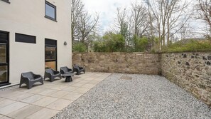 A patio area with outdoor seating, a stone wall, and a building with windows and a door. - Student Only Straits Place (Edinburgh)