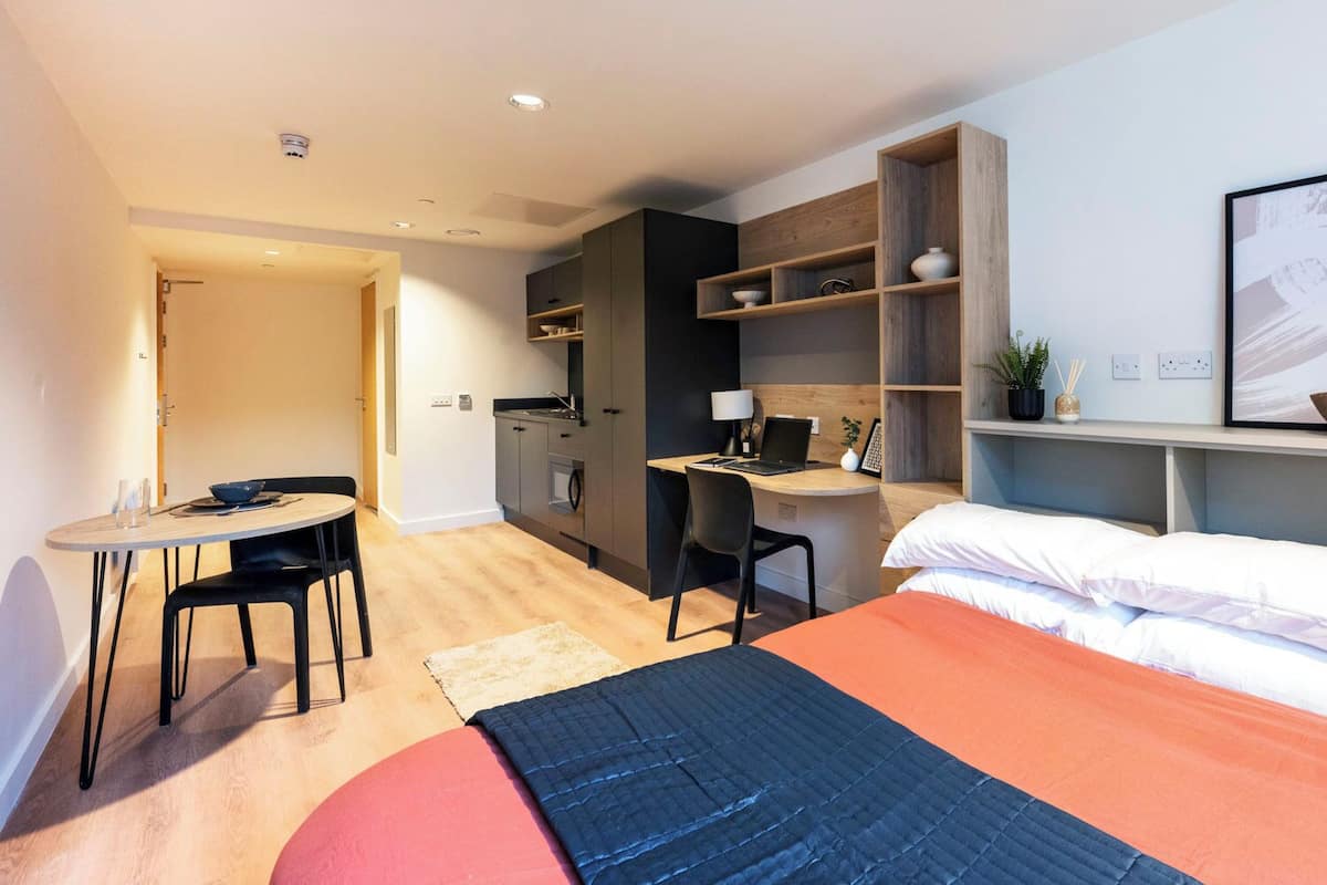 Una habitación de hotel moderna con cama, escritorio, silla, kitchenette y una pequeña mesa de comedor.