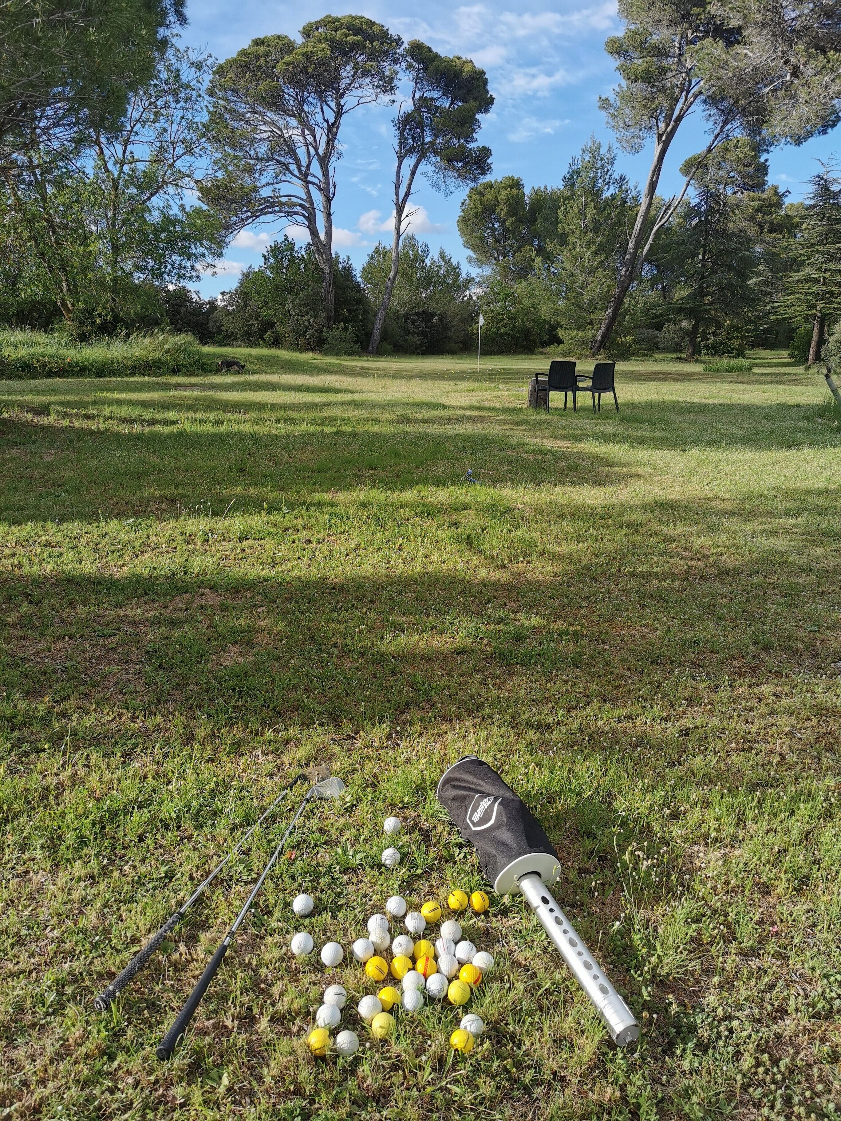 Un campo de golf con un putting green, una bandera y un par de sillas al fondo.