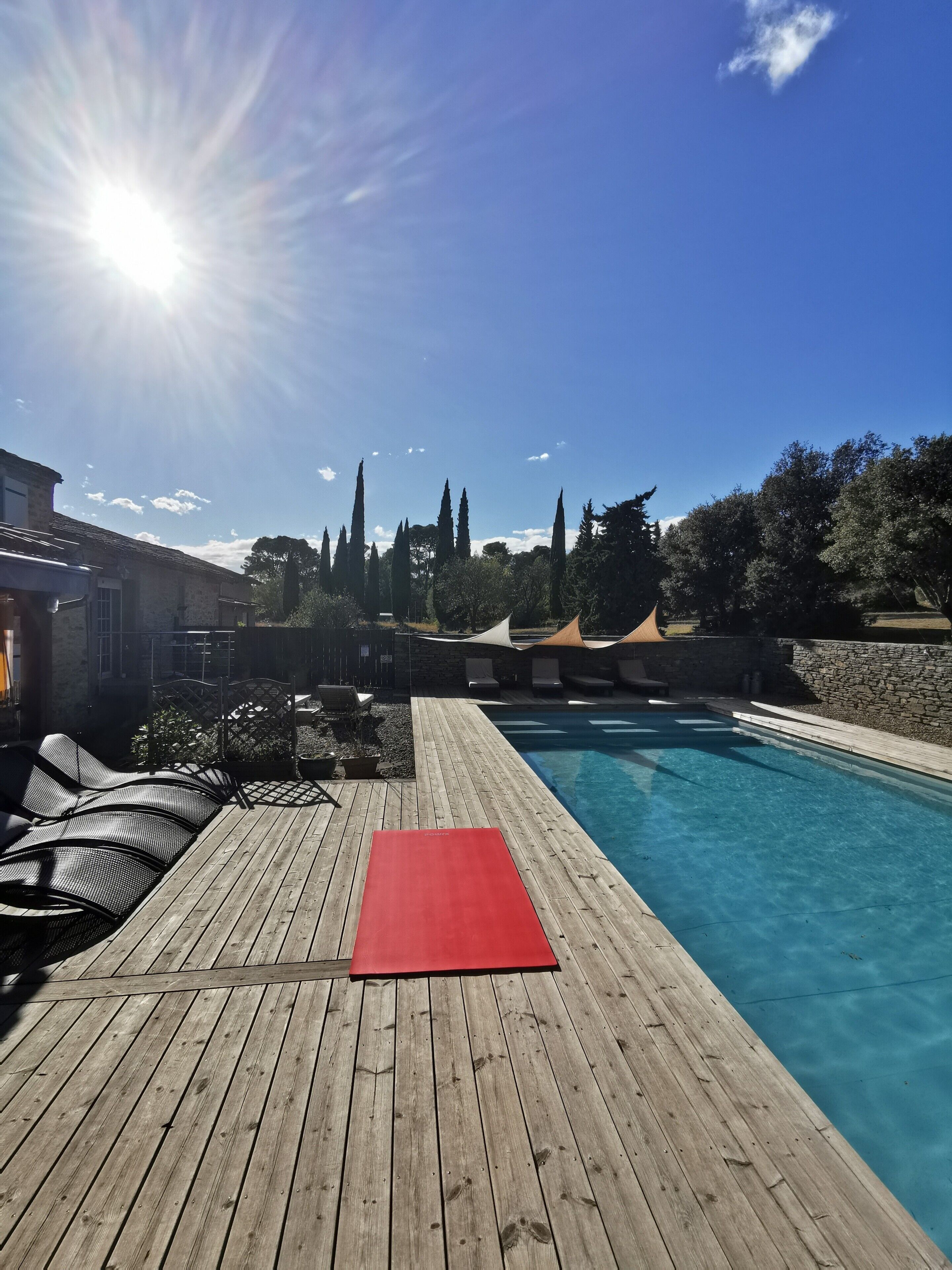 A wooden deck with a red mat, a swimming pool, and a stone wall.