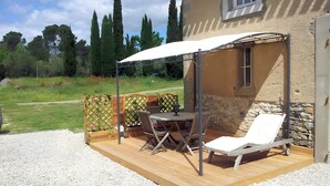 A covered patio with a table and chairs, a lounge chair, and a stone wall.