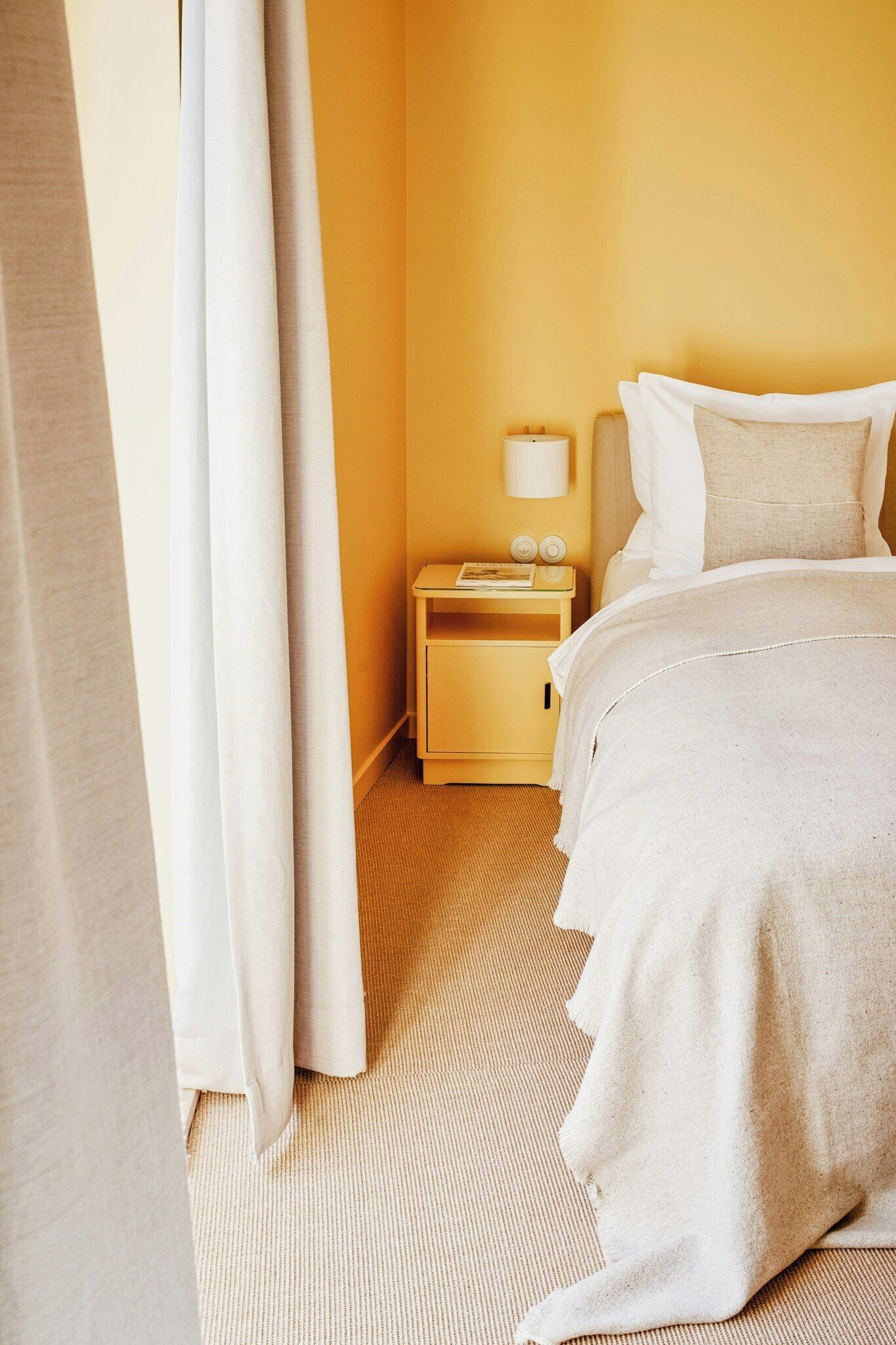 Una habitación de hotel con cama, mesita de noche, lámpara y cortinas.