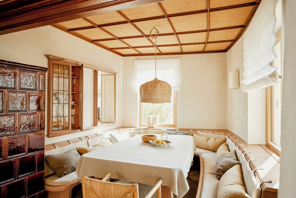 A dining area with a large table, cushioned seating, a hanging light fixture, and a window with natural light. - Architectural gem with sea view (Norderney)
